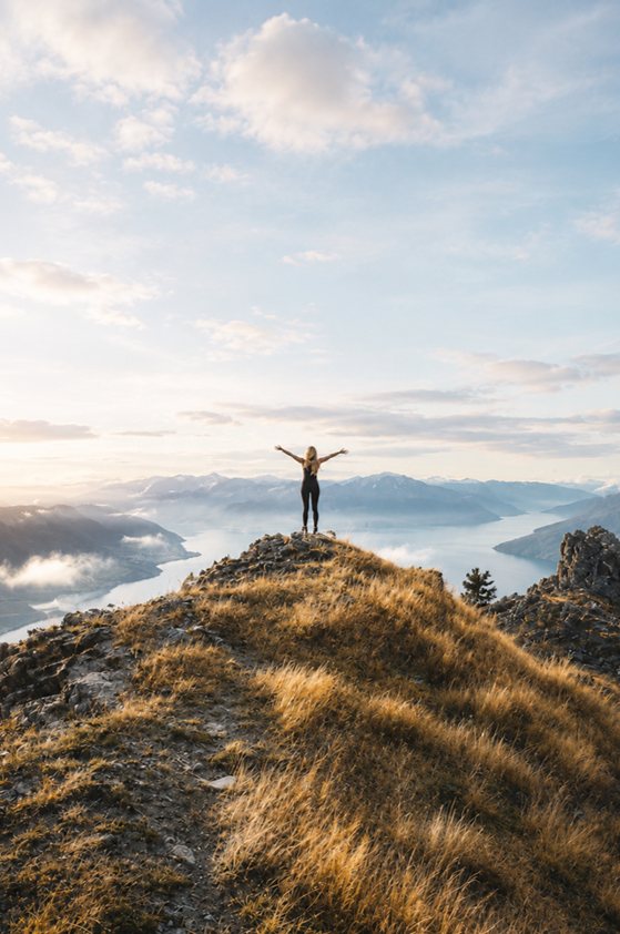 A person standing on a misty mountain summit at sunrise, arms raised